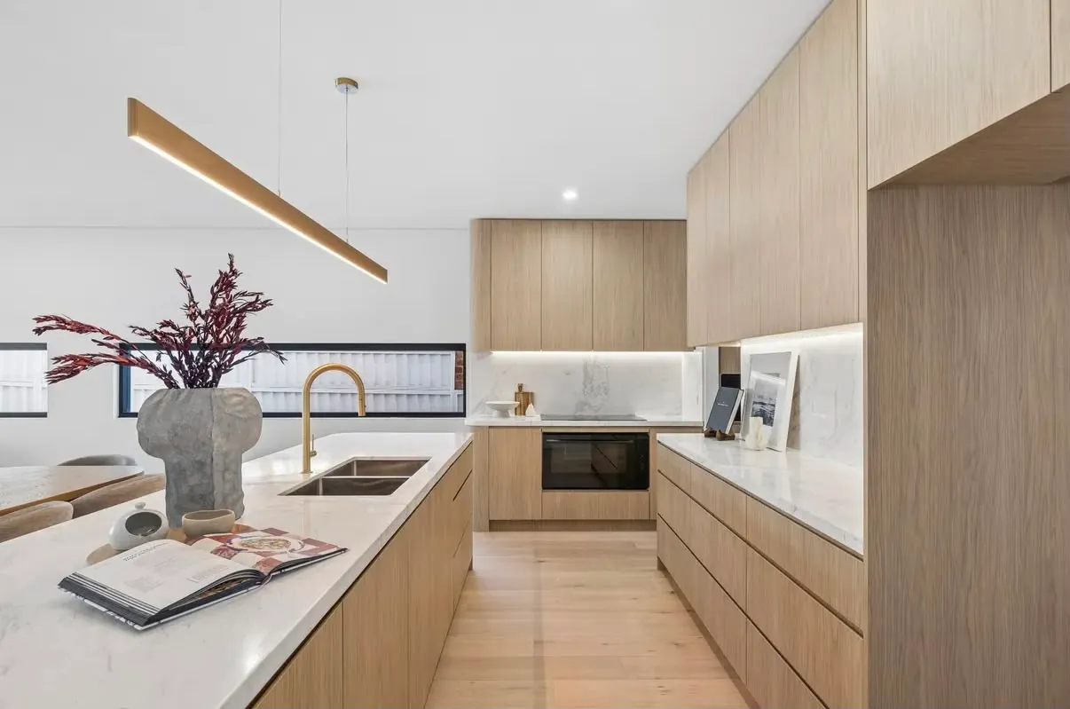 Kitchen with timber-look cabinetry, a long stone island with a brass tap and a lit stone splashback