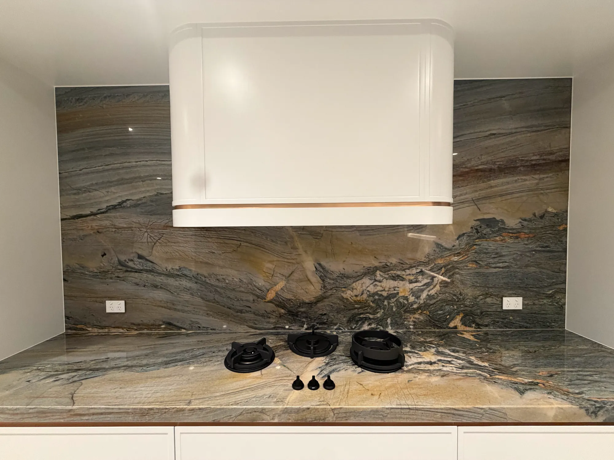 Gas cooktop set into a veined stone benchtop with a matching full-height splashback and a curved white rangehood surround